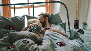 A couple plays the Arcana of Love couples game while lounging in bed.